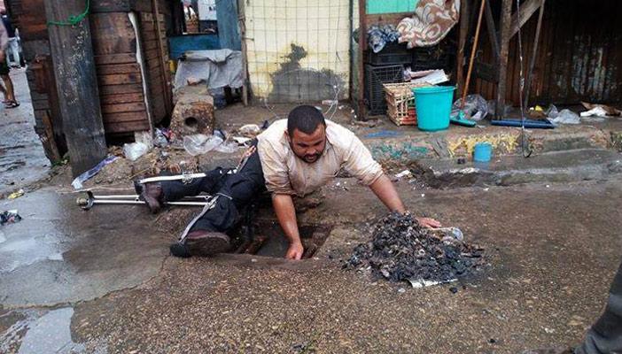 بالصور.. مُعاق يقوم بإصلاح بالوعة الشارع لاستيعاب الأمطار في البحيرة